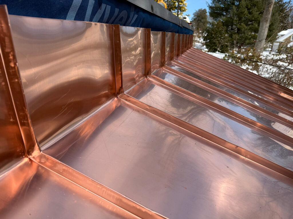 Copper double locked roof pans seamlessly turned up the wall.